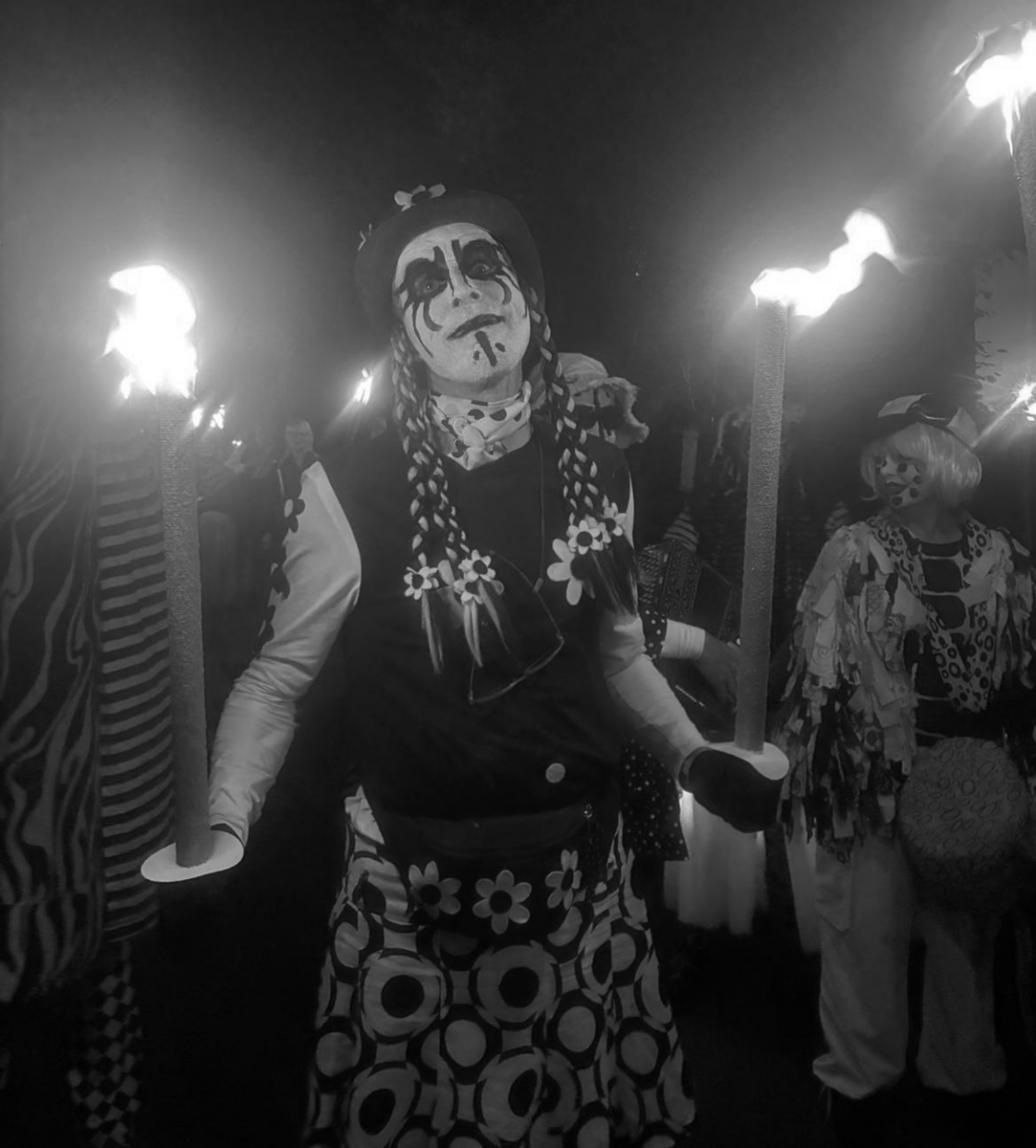 Pig Dyke Molly dancer holding two flaming torches in the night time parade at the Sidmouth Folk Festival in 2025